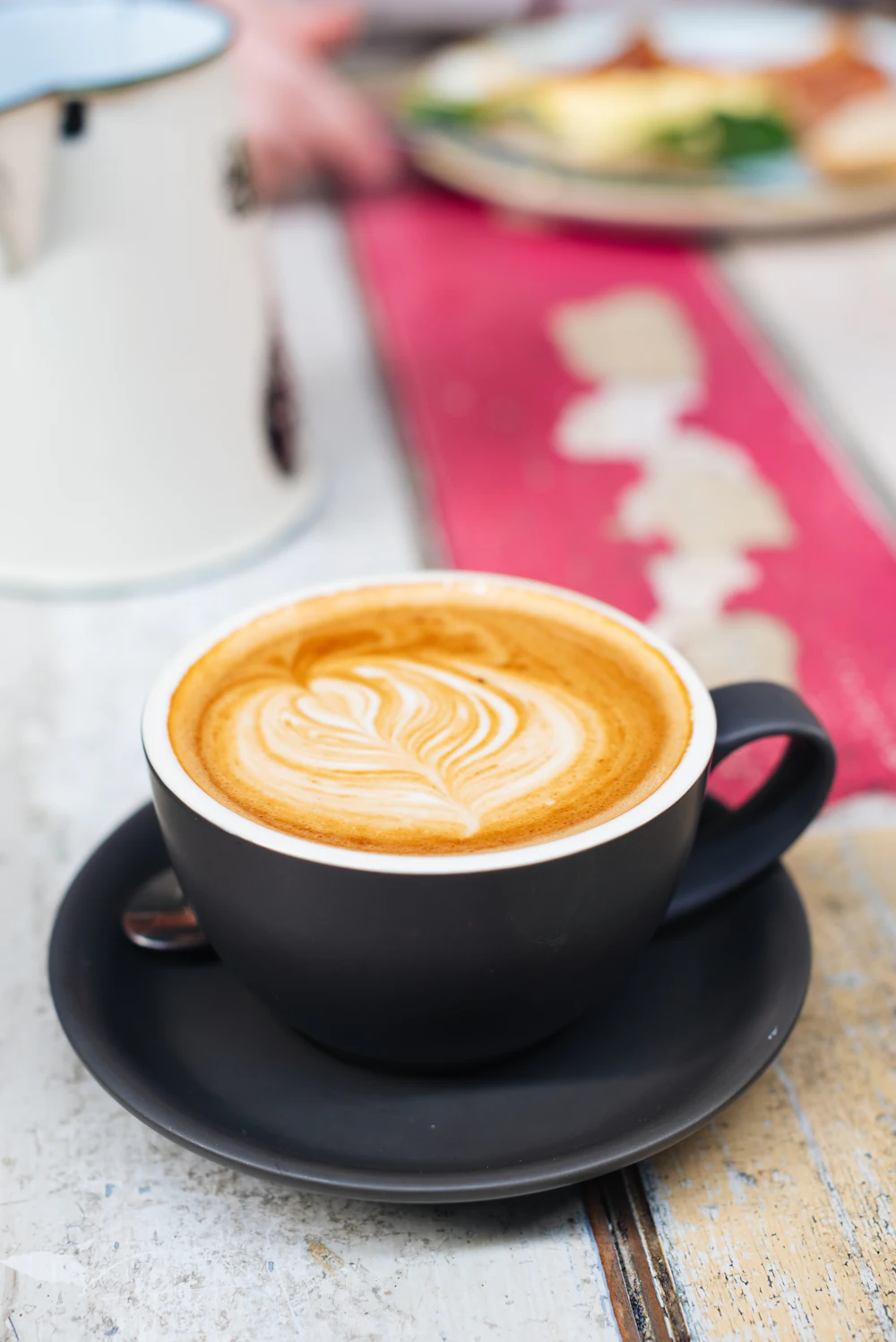 Flat white with latte art in a black cup on a timber bench